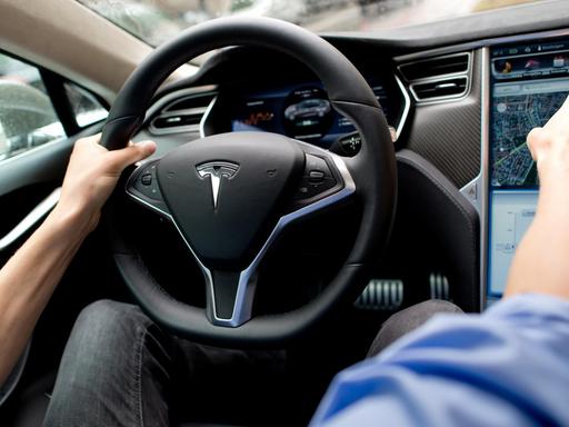Ein Mann sitzt in einem Tesla Model S auf dem Fahrersitz vor einem Showroom des Autoherstellers.