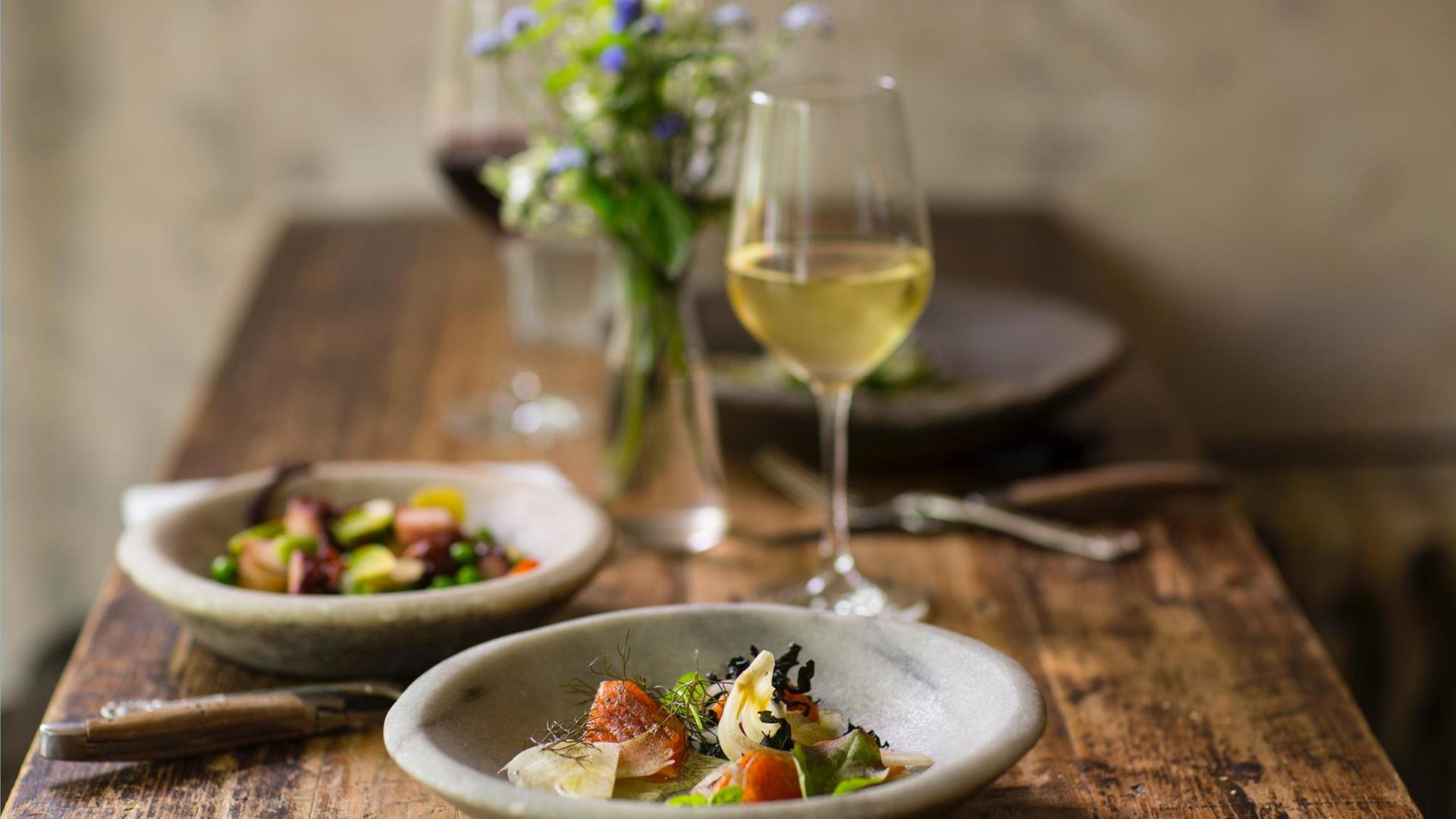 Auf einem Tisch stehen Schüsseln mit Salat, Weingläser und ein Vase mit Blumen. Auf einem Tisch stehen Schüsseln mit Salat, Weingläser und ein Vase mit Blumen.