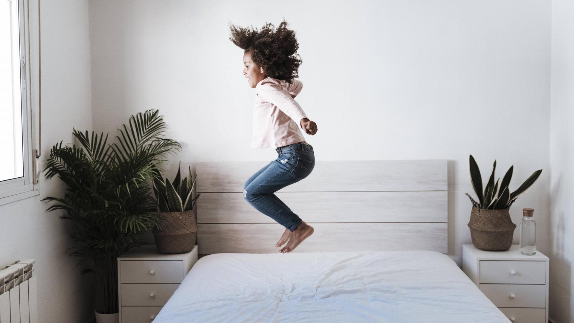 Ein Mädchen hüpft auf einem Bett.