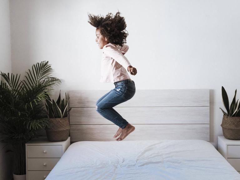 Ein Mädchen hüpft auf einem Bett.