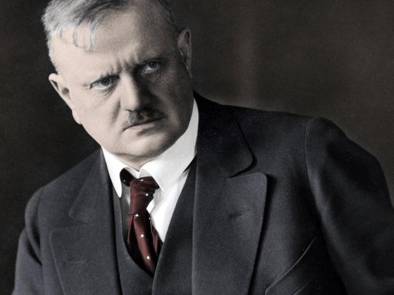 Nachkoloriertes Foto des sitzenden Komponisten Jean Sibelius, der etwas grimmig zur Seite schaut.