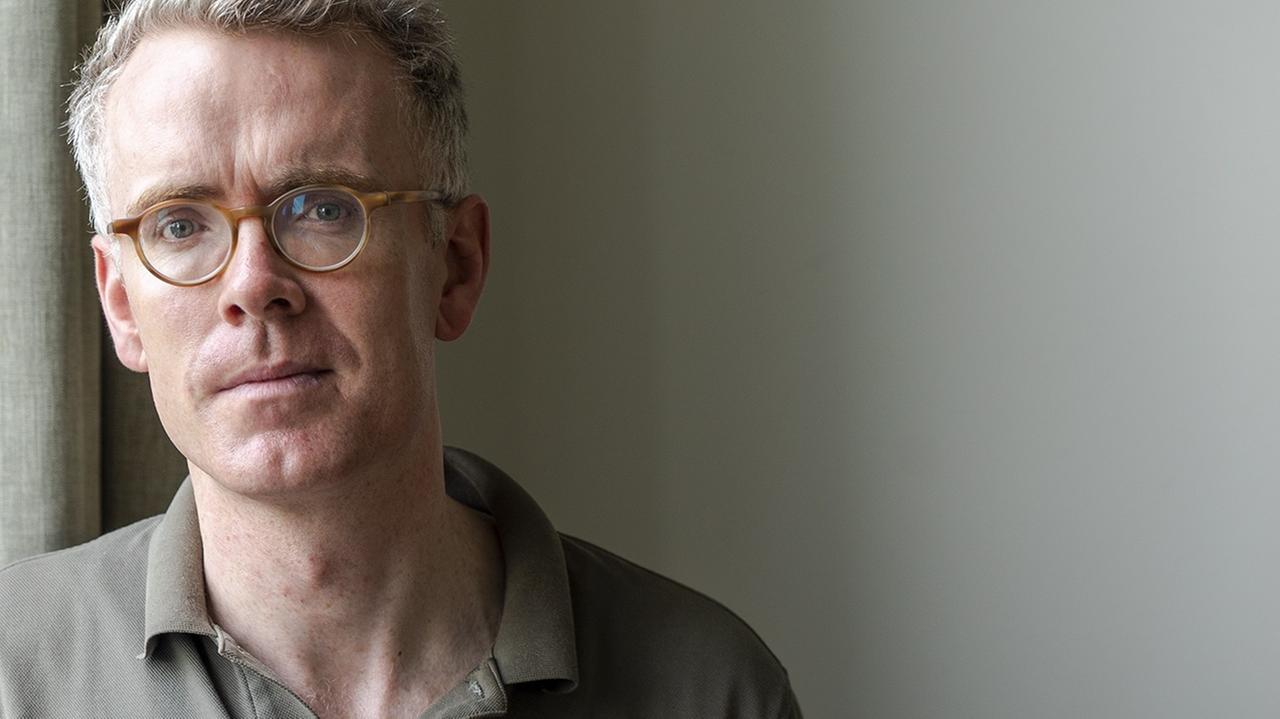 Derek Scally trägt Brille, steht am Fenster und schaut in die Kamera. Derek Scally trägt Brille, steht am Fenster und schaut in die Kamera.