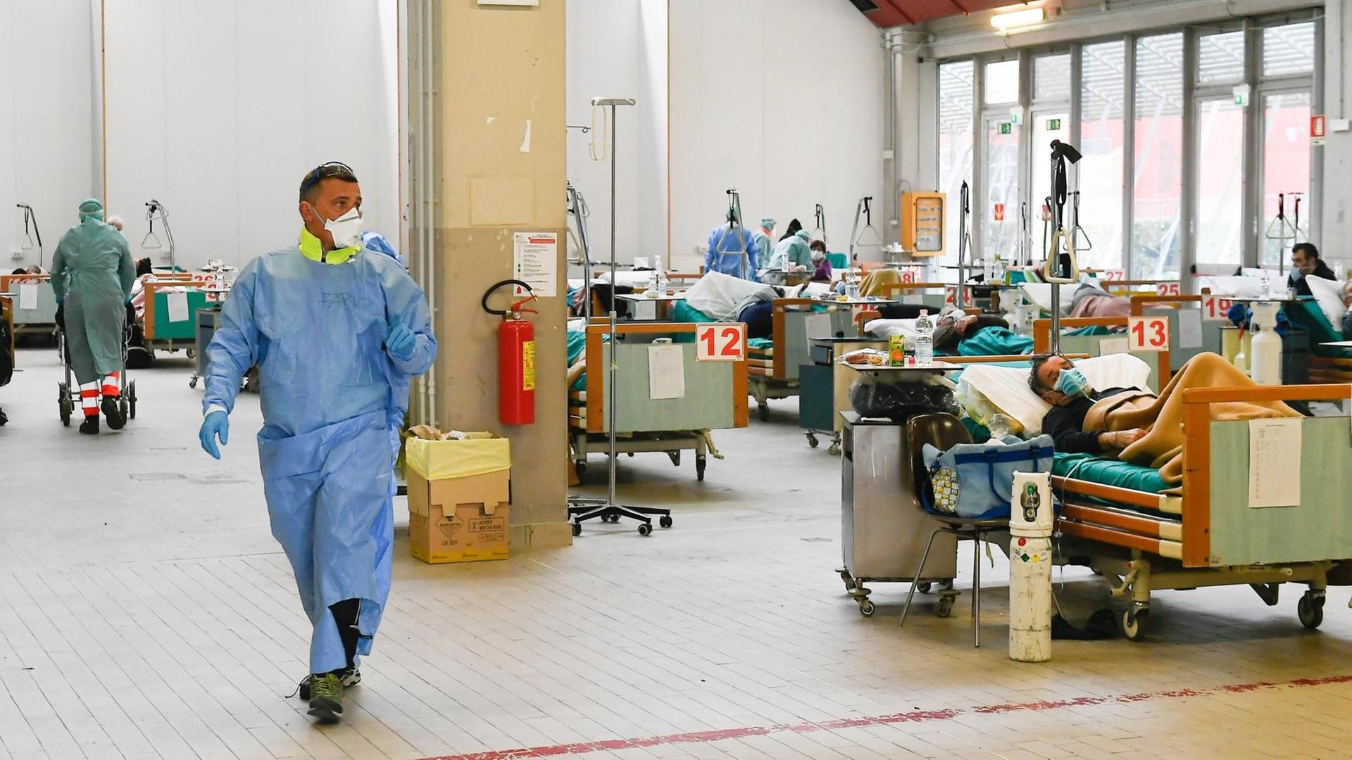 Die Covid-19-Station in einem italienischen Krankenhaus. Patienten liegen in nummerierten Betten. Ein Mann, vermutlich Arzt oder Pfleger, läuft durch den Raum. Die Covid-19-Station in einem italienischen Krankenhaus. Patienten liegen in nummerierten Betten. Ein Mann, vermutlich Arzt oder Pfleger, läuft durch den Raum.