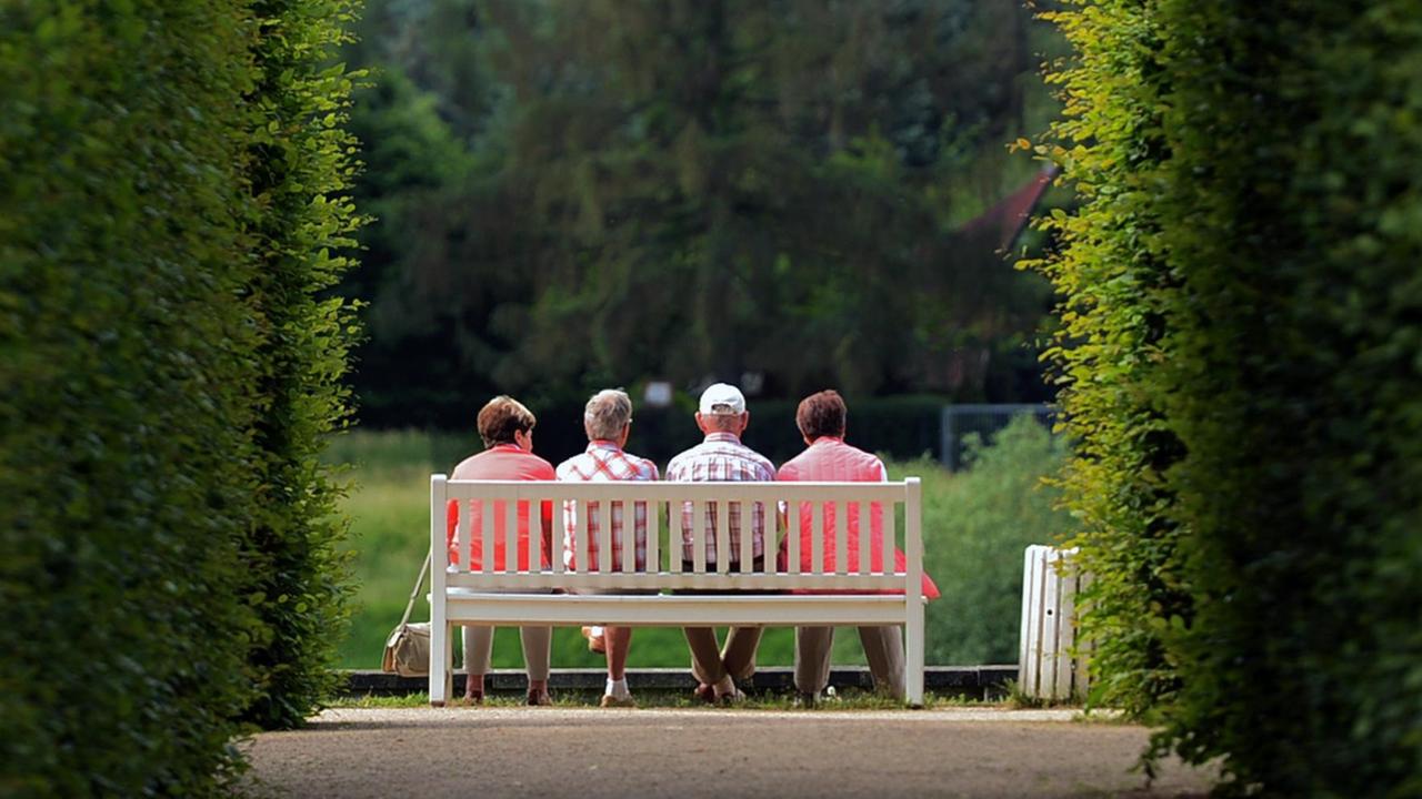 Mehrere ältere Personen sitzen am auf einer Parkbank im Schlosspark Pillnitz (Sachsen).