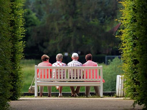 Mehrere ältere Personen sitzen am auf einer Parkbank im Schlosspark Pillnitz (Sachsen).