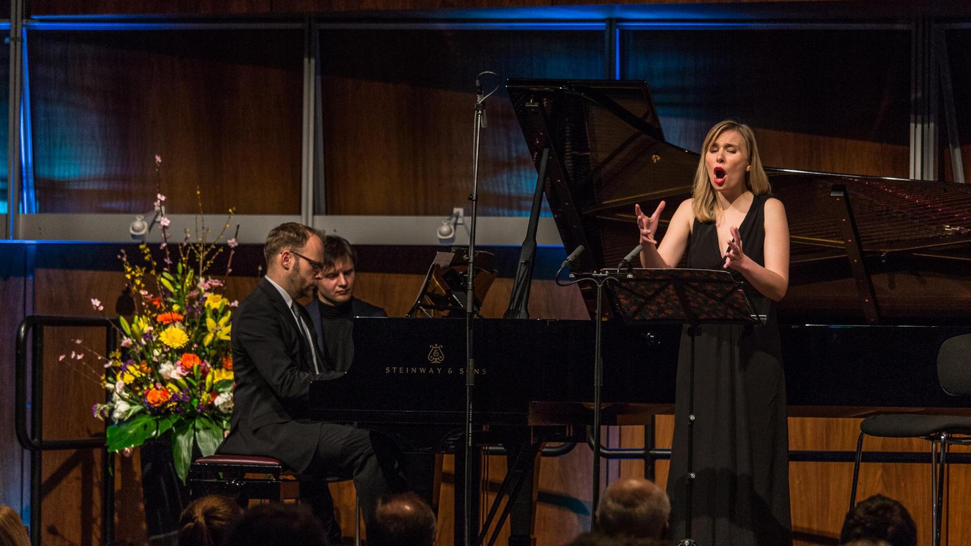 Sopranistin Elsa Dreisig steht singend vor einem Notenpult. Pianist Jonathan Ware sitzt am Flügel. Im Hintergrund ein Blumengesteck und die Holzvertäfelung des Deutschlandfunk Kammermusiksaals. Sopranistin Elsa Dreisig steht singend vor einem Notenpult. Pianist Jonathan Ware sitzt am Flügel. Im Hintergrund ein Blumengesteck und die Holzvertäfelung des Deutschlandfunk Kammermusiksaals.
