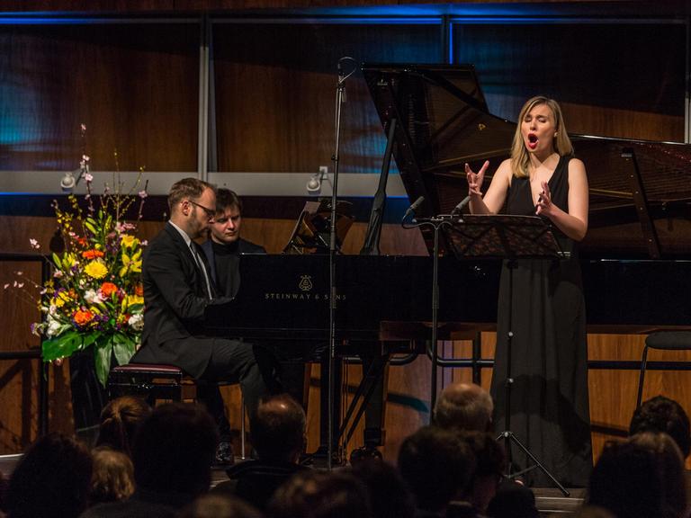 Sopranistin Elsa Dreisig steht singend vor einem Notenpult. Pianist Jonathan Ware sitzt am Flügel. Im Hintergrund ein Blumengesteck und die Holzvertäfelung des Deutschlandfunk Kammermusiksaals.