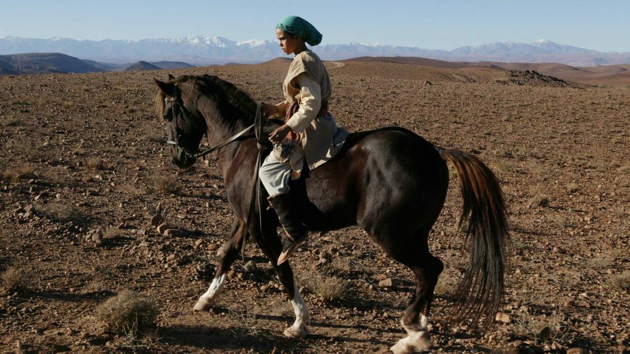 Bild aus dem Film "Zaina - Königin der Pferde". Das Mädchen Zaina sitzt auf einem PFerd und reitet durch die Wüste. Bild aus dem Film "Zaina - Königin der Pferde". Das Mädchen Zaina sitzt auf einem PFerd und reitet durch die Wüste.