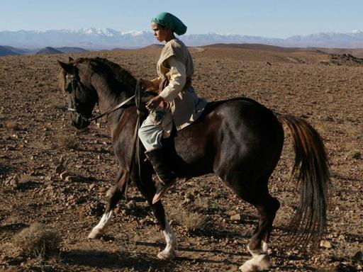 Bild aus dem Film "Zaina - Königin der Pferde". Das Mädchen Zaina sitzt auf einem PFerd und reitet durch die Wüste.