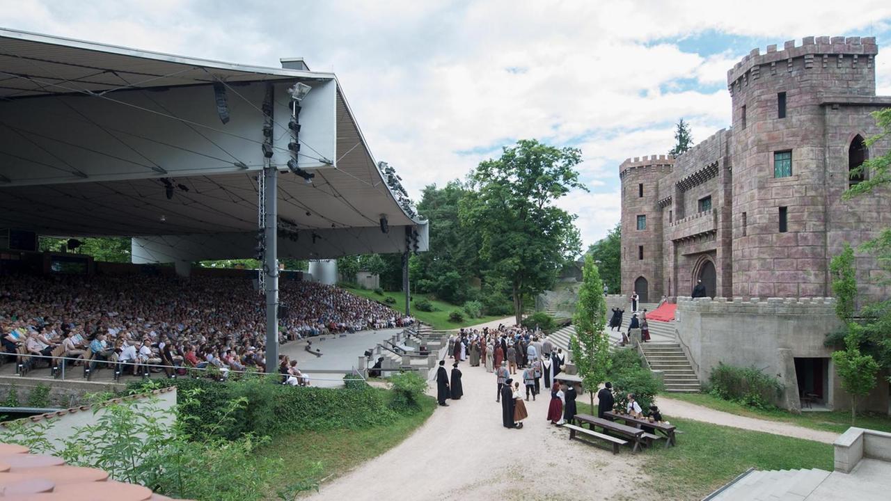 Panorama einer großen Freilichtbühne mit einem großen, überdachten Zuschauerraum und einer Burg, die den Schauspielern als Kulisse dient. Panorama einer großen Freilichtbühne mit einem großen, überdachten Zuschauerraum und einer Burg, die den Schauspielern als Kulisse dient.