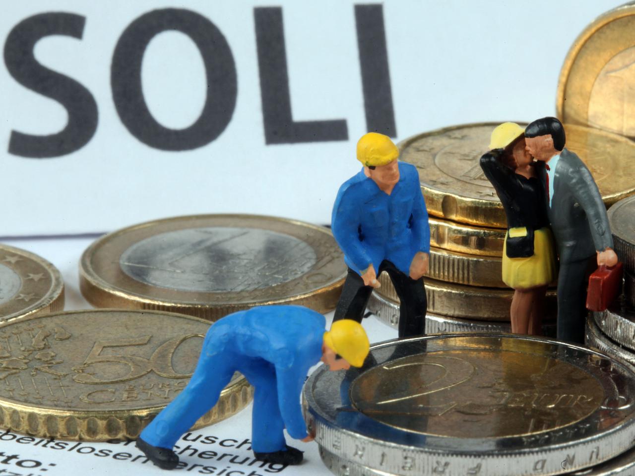Modellfiguren inmitten von Euromünzen, im Hintergrund steht "Soli" geschrieben. Modellfiguren inmitten von Euromünzen, im Hintergrund steht "Soli" geschrieben.