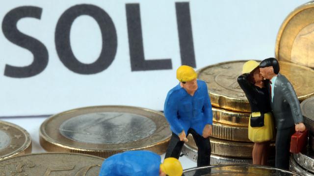 Modellfiguren inmitten von Euromünzen, im Hintergrund steht "Soli" geschrieben.