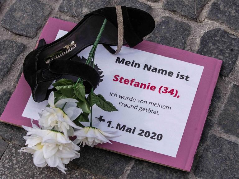 Proteste gegen Femizide: Auf einem Schild steht "Mein Name ist Stefanie (34) ich wurde von meinem Freund getötet". Daneben liegt auf dem Boden ein Schuh und eine weiße Blume.