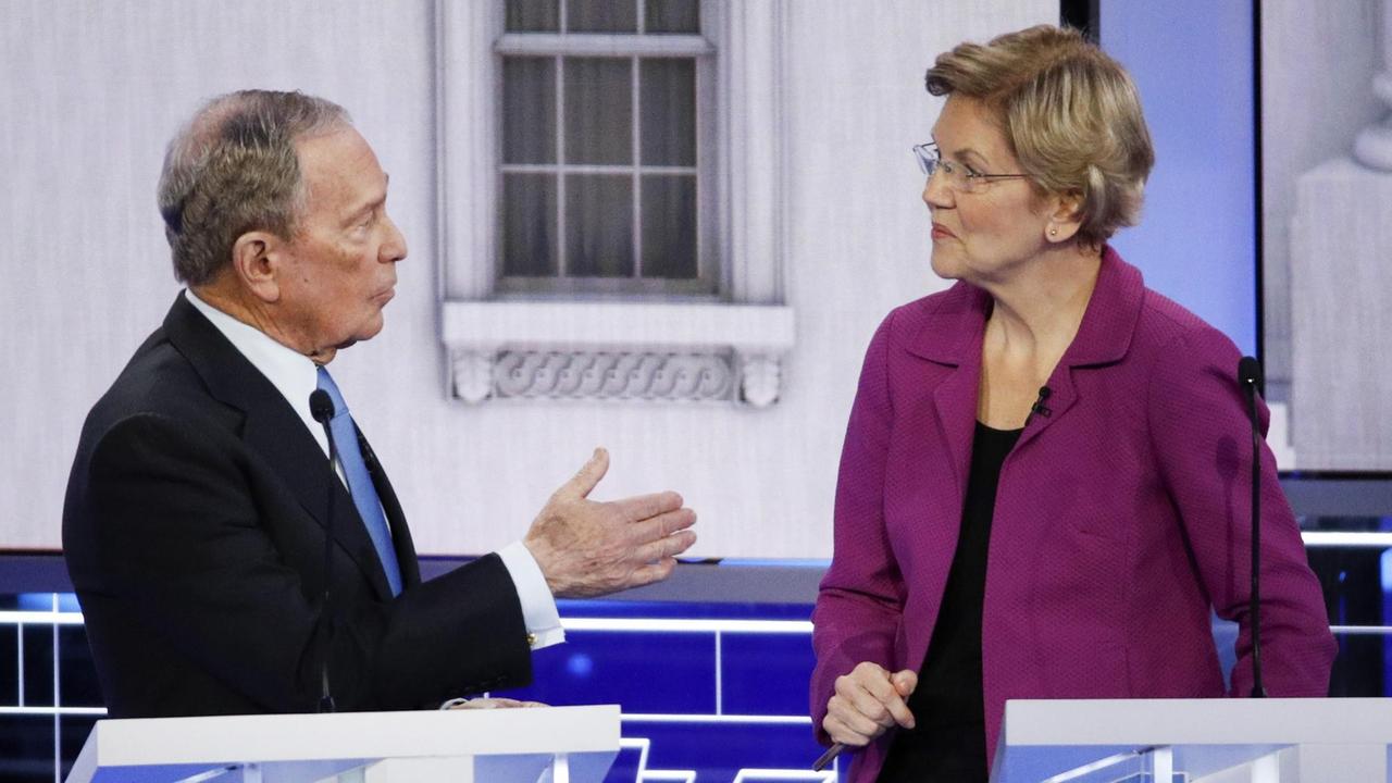 Die beiden sind einander zugeneigt. Bloomberg spricht zu Warren und gestikuliert mit der rechten Hand. Die beiden sind einander zugeneigt. Bloomberg spricht zu Warren und gestikuliert mit der rechten Hand.