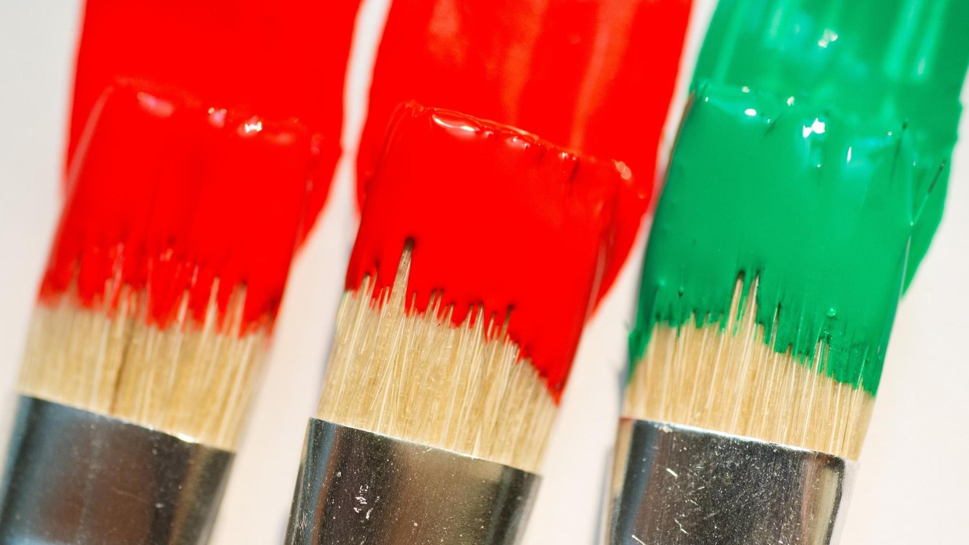 Pinsel mit roter, roter und grüner Farbe liegen auf einem weißen Blatt Papier. Pinsel mit roter, roter und grüner Farbe liegen auf einem weißen Blatt Papier.