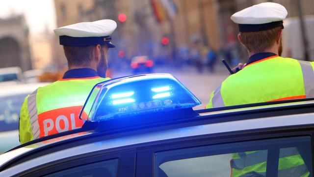 Polizisten stehen neben einem Einsatzwagen der Polizei mit eingeschaltetem Blaulicht