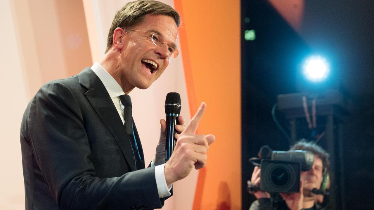 Mark Rutte feiert seinen Wahlsieg vor Anhängern in Den Haag. Er steht auf einer Bühne vor dem organgefarbenen Emblem seiner Partei. Mark Rutte feiert seinen Wahlsieg vor Anhängern in Den Haag. Er steht auf einer Bühne vor dem organgefarbenen Emblem seiner Partei.