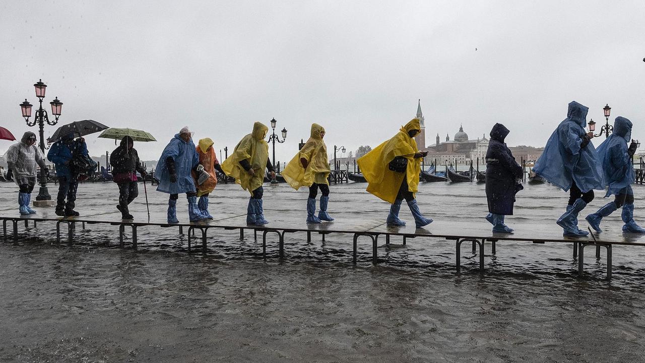Touristen spazieren am 12. November 2019 in Venedig, Italien, auf der Piazza San Marco im Hochwasser. Touristen spazieren am 12. November 2019 in Venedig, Italien, auf der Piazza San Marco im Hochwasser.