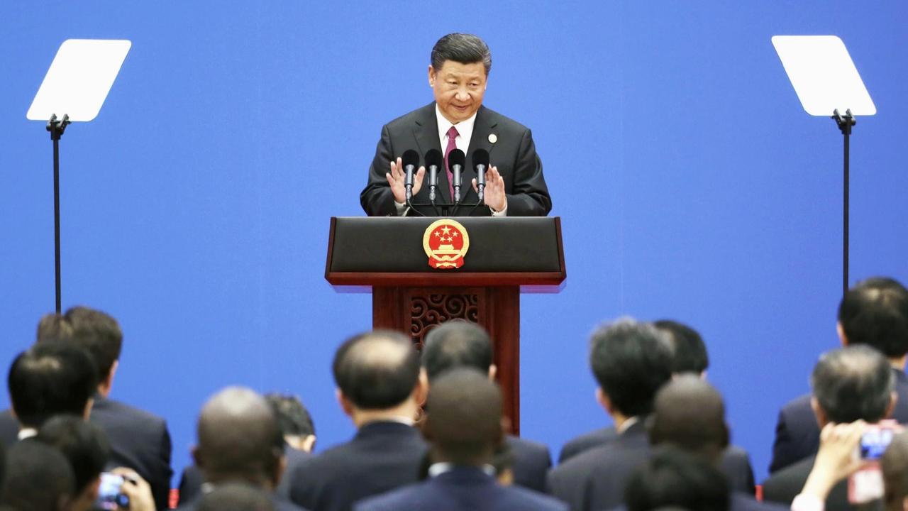 Der chinesische Staatspräsident Xi Jinping steht redend und gestikulierend hinter einem Pult und spricht zu einer Menschenmenge vor ihm. Der chinesische Staatspräsident Xi Jinping steht redend und gestikulierend hinter einem Pult und spricht zu einer Menschenmenge vor ihm.