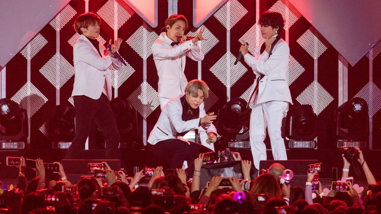 Vier Männer der Band BTS singen vor Publikum. Vier Männer der Band BTS singen vor Publikum.