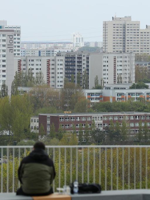 Ein Mann sitzt allein auf einer Terrasse und schaut zu den Plattenbauten von Marzahn hinüber, die zu DDR-Zeiten errichtet wurden.