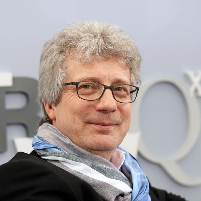 Ein Mann mit grauen Haaren und einer Brille sitzt auf einem Sofa. Ein Mann mit grauen Haaren und einer Brille sitzt auf einem Sofa.