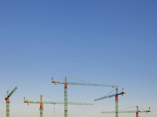 Baukräne in Berlin recken sich in den blauen Himmel.