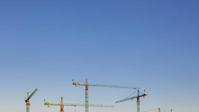 Baukräne in Berlin recken sich in den blauen Himmel.