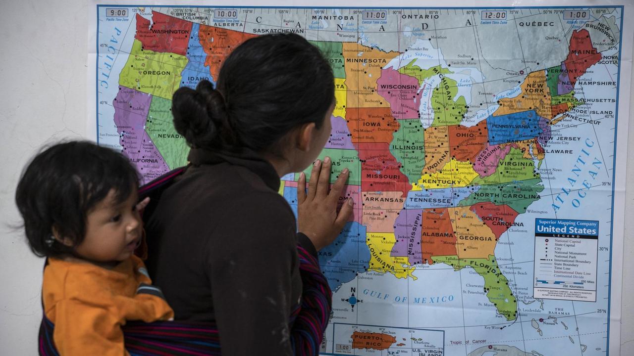 Ein Frau aus Guatemala, die ihr Kind in einem Tragetuch auf dem Rücken trägt, schaut auf eine Karte der USA; Zentrum für Flüchtlinge der Hilfsorganisation Annunciation House