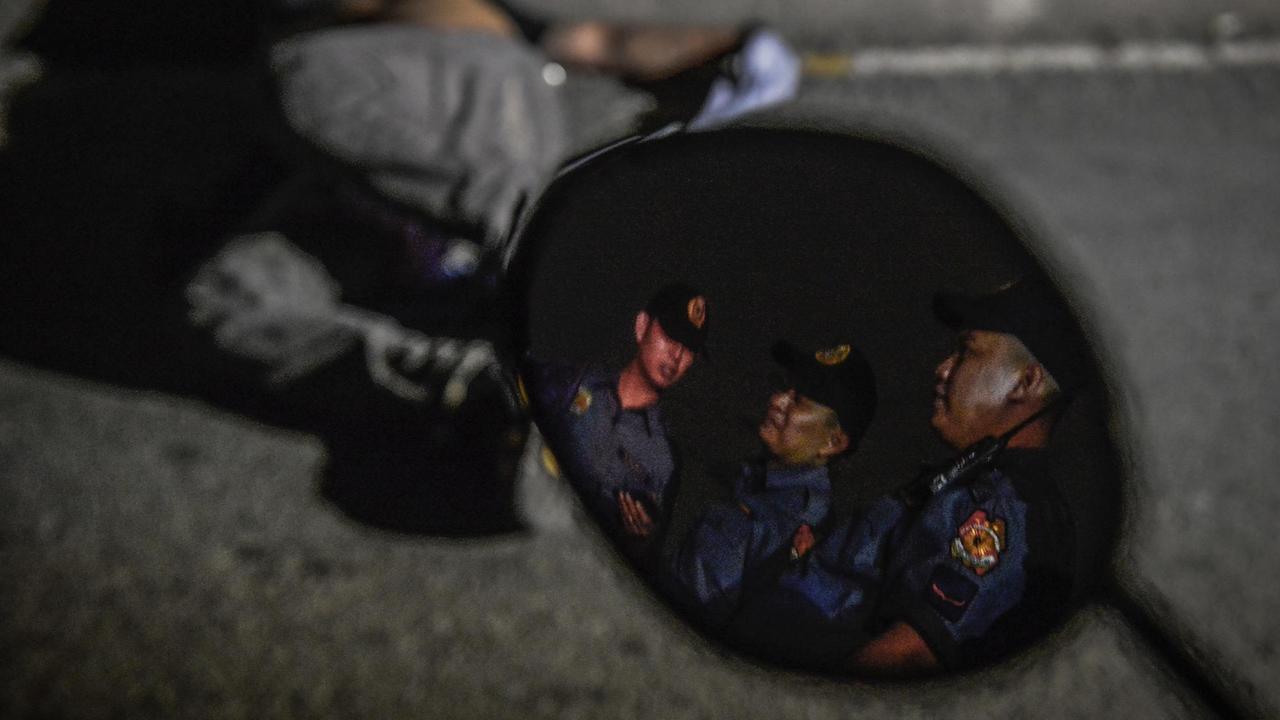 Polizisten spiegeln sich in einem Mofa-Spiegel, während sie den Körper eines Erschossenen in Manila, Philippinen, bewachen (2017). Der von Präsident Rodrigo Duterte ausgerufene "Kampf gegen Drogen" hat Tausende Todesopfer gefordert.