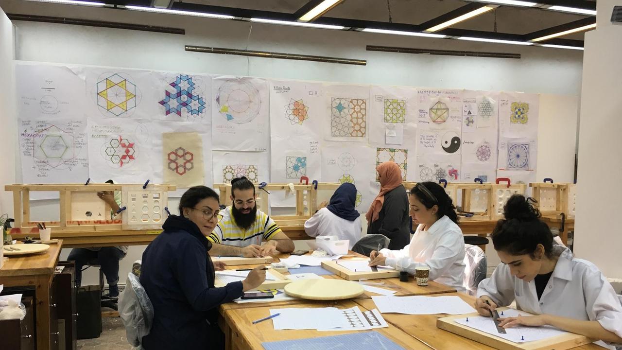 Frauen und Männer sitzen an Tischen und arbeiten zusammen in einer Kunsthochschule in Jeddah, Saudi-Arabien.
