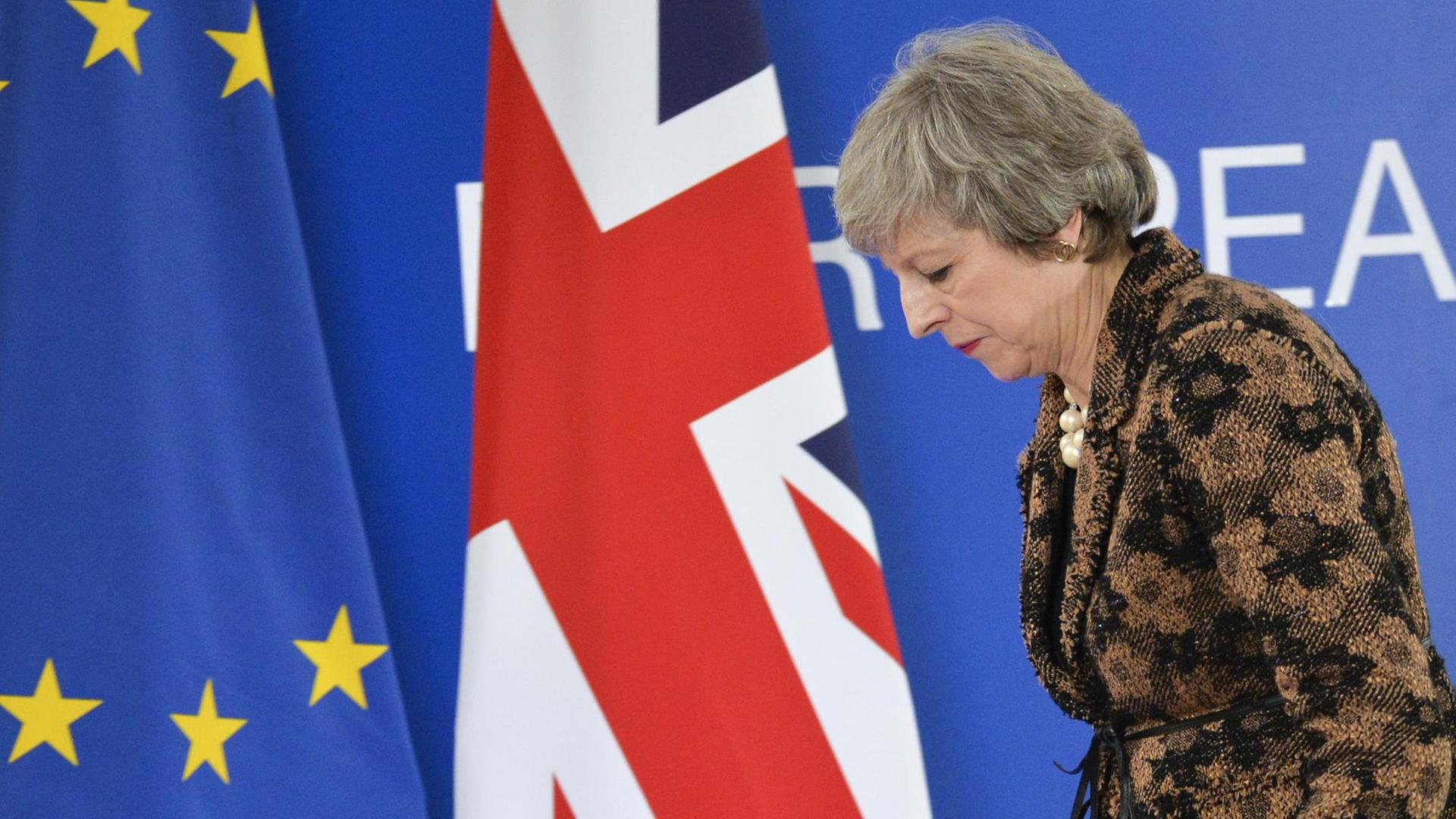 May läuft gebeugt an einer EU- und einer Gr0ßbritannien-Flagge vorbei. May läuft gebeugt an einer EU- und einer Gr0ßbritannien-Flagge vorbei.
