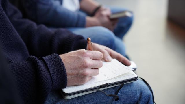 Ein Mann schreibt mit einem Stift in seinen Notitzblock.