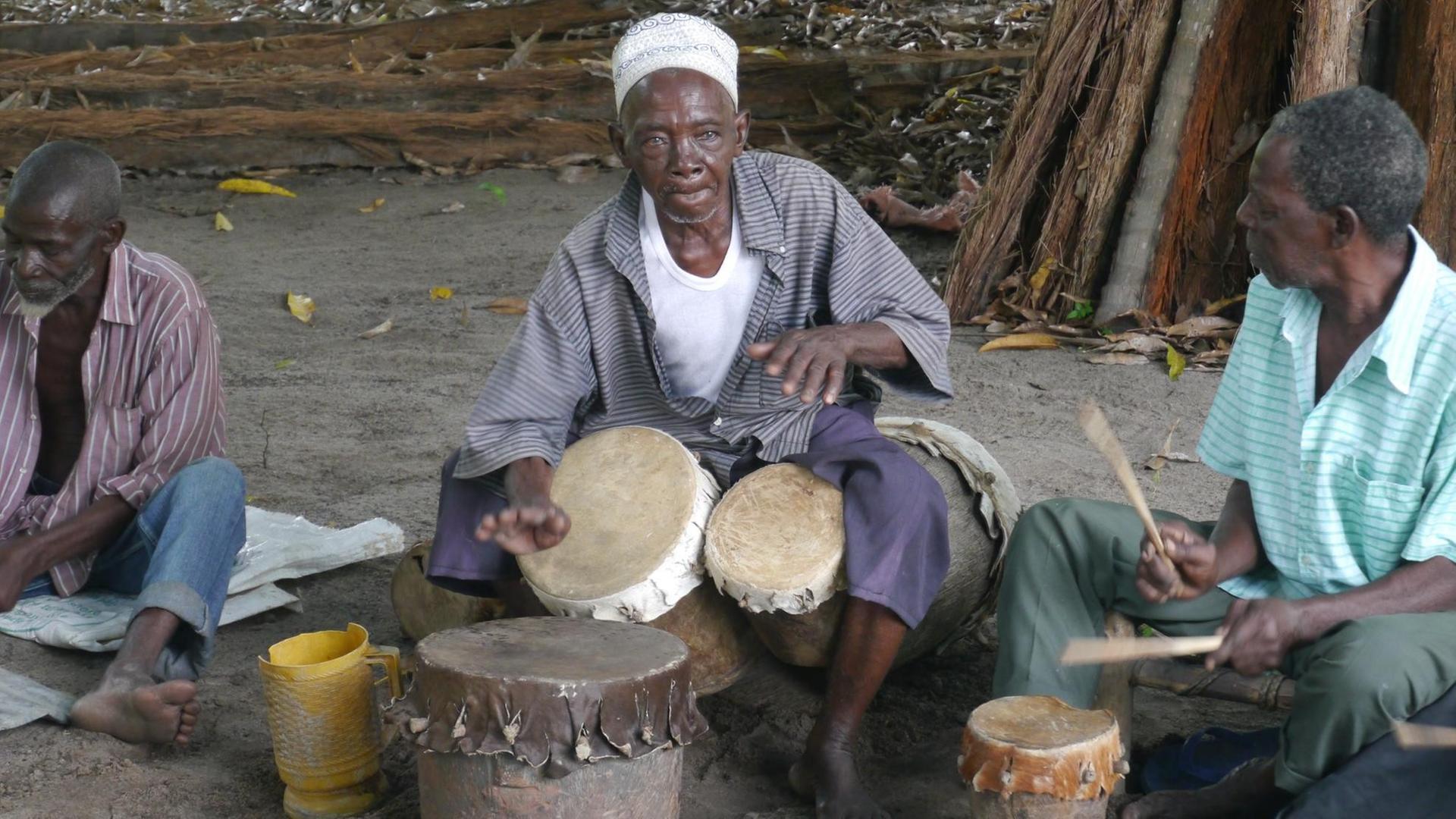 Drei Männer mit ihren Trommeln sitzen in Bagamoyo in Tansania an einer Straße Drei Männer mit ihren Trommeln sitzen in Bagamoyo in Tansania an einer Straße