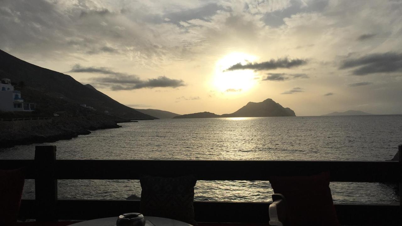 Die große strahlende Sonne versinkt auf der anderen Seite des Meeres zwischen den Wolken und hinter einem Felsen ins Wasser. Die große strahlende Sonne versinkt auf der anderen Seite des Meeres zwischen den Wolken und hinter einem Felsen ins Wasser.