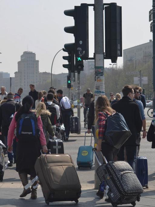 Touristen ziehen am Berliner Alexanderplatz Rollkoffer hinter sich her.