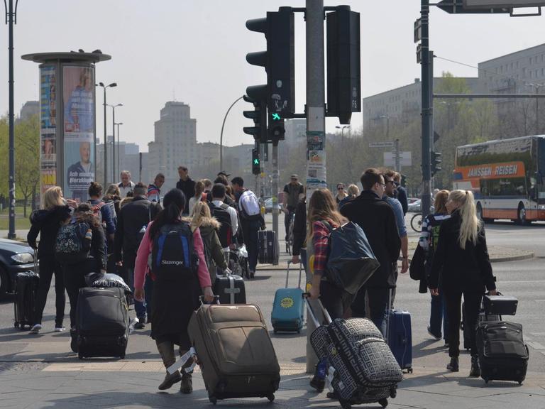Touristen ziehen am Berliner Alexanderplatz Rollkoffer hinter sich her.