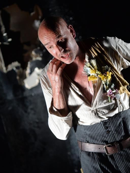 Paul Herwig als Georg Trakl in "Der Abschied", Schauspieler mit Glatze, hellem aufgerissenen Hemd und grauer Hose auf einer dunklen Bühne