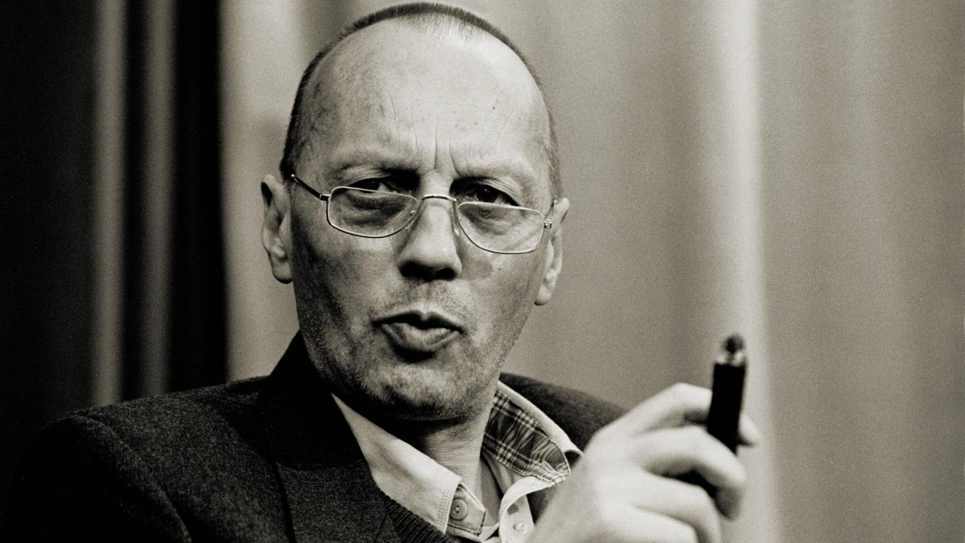 Schwarzweißporträt von Karl Mickel, der mit ernster Miene und einer Zigarre in der Hand in die Kamera blickt. Schwarzweißporträt von Karl Mickel, der mit ernster Miene und einer Zigarre in der Hand in die Kamera blickt.