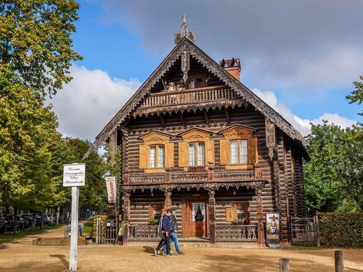 Ein Holzhaus in der Russischen Kolonie Alexandrowka in Potsdam. Davor sind zwei Spaziergänger.