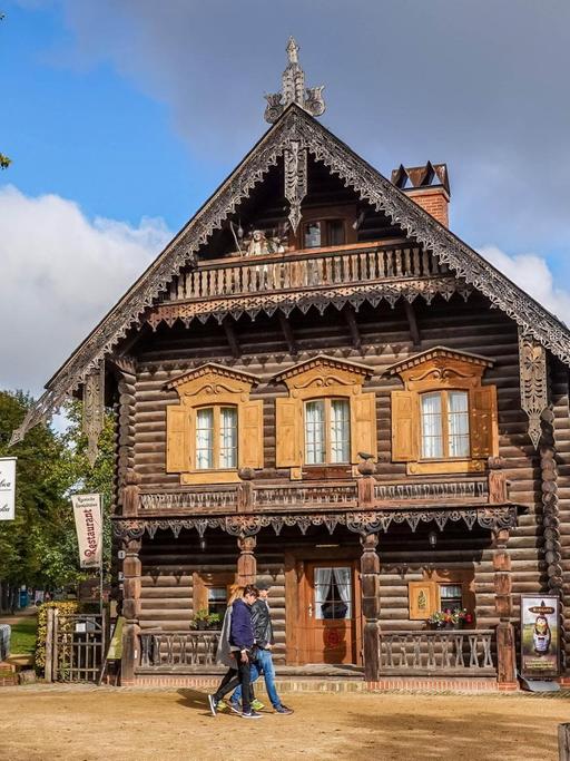 Ein Holzhaus in der Russischen Kolonie Alexandrowka in Potsdam. Davor sind zwei Spaziergänger.
