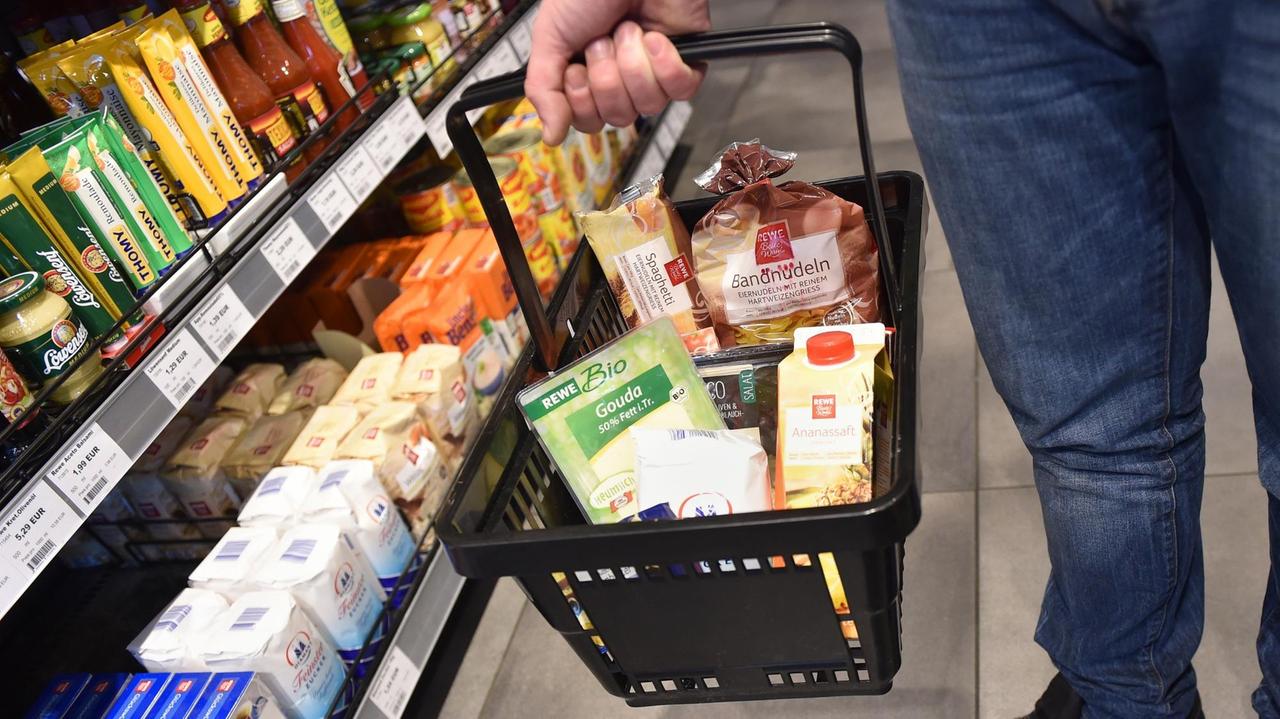 Mann mit einem Einkaufskorb steht zwischen Lebensmittel-Regalen
