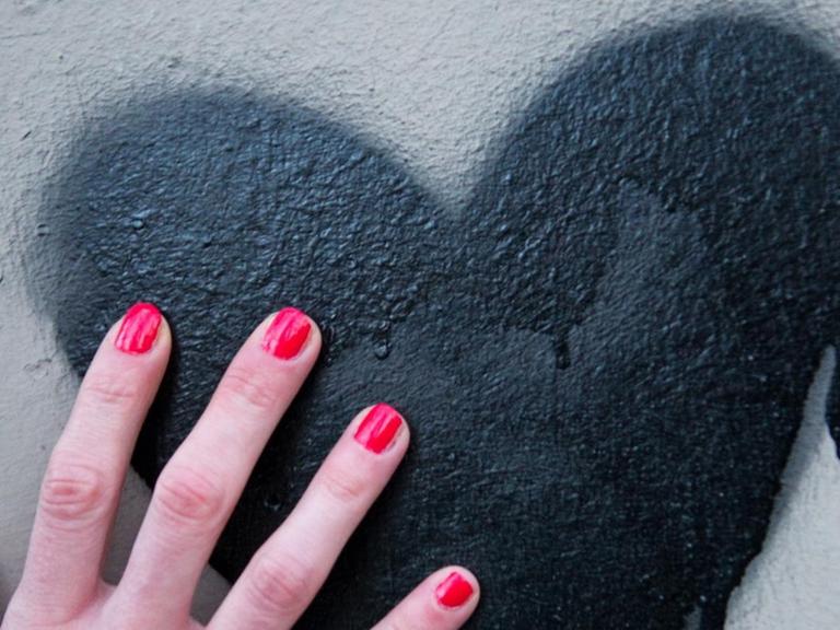 Eine Frauenhand mit rot lackierten Fingernägeln berührt am 03.03.2014 in Berlin ein schwarzes Herz, das auf eine Mauer gespüht wurde.