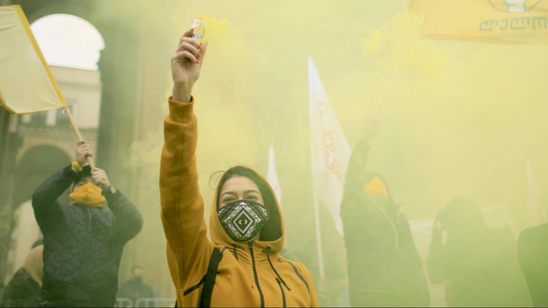 Eine junge Frau in gelber Jacke reckt bei einer Demonstration den Arm in die Höhe. Eine junge Frau in gelber Jacke reckt bei einer Demonstration den Arm in die Höhe.