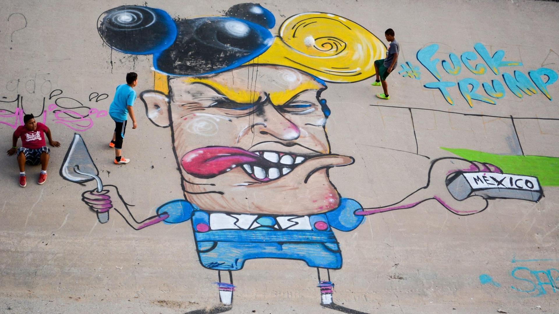 Kinder spielen am 23.06.2016 neben einer Graffiti-Karikatur des designierten US-Präsidenten Donald Trump im Flussbett des Rio Grande (Rio Bravo in Mexiko). Ein Streetart-Künstler sprayte die neun Meter große Karikatur an die Wand des zubetonierten Kanals an der Grenze zwischen Mexiko und den USA in der Stadt Ciudad Juarez. Kinder spielen am 23.06.2016 neben einer Graffiti-Karikatur des designierten US-Präsidenten Donald Trump im Flussbett des Rio Grande (Rio Bravo in Mexiko). Ein Streetart-Künstler sprayte die neun Meter große Karikatur an die Wand des zubetonierten Kanals an der Grenze zwischen Mexiko und den USA in der Stadt Ciudad Juarez.