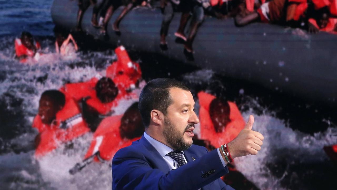 Italiens Innenminister Matteo Salvini in einer Ferhsehdiskussion in Rom vor einem Bildschirm mit Schlauchboot und Flüchtingen, Juni 2018 Italiens Innenminister Matteo Salvini in einer Ferhsehdiskussion in Rom vor einem Bildschirm mit Schlauchboot und Flüchtingen, Juni 2018