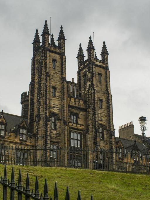 Blick auf das historische Gebäude des New College der University of Edinburgh, dahinter ein grauer Wolkenhimmel.