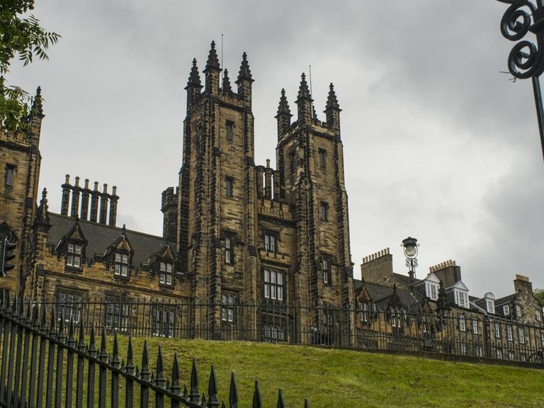 Blick auf das historische Gebäude des New College der University of Edinburgh, dahinter ein grauer Wolkenhimmel.