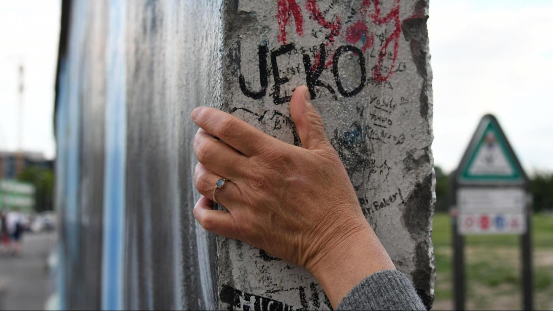 Eine Hand umgreift ein erhaltenes Teilstück der Berliner Mauer.