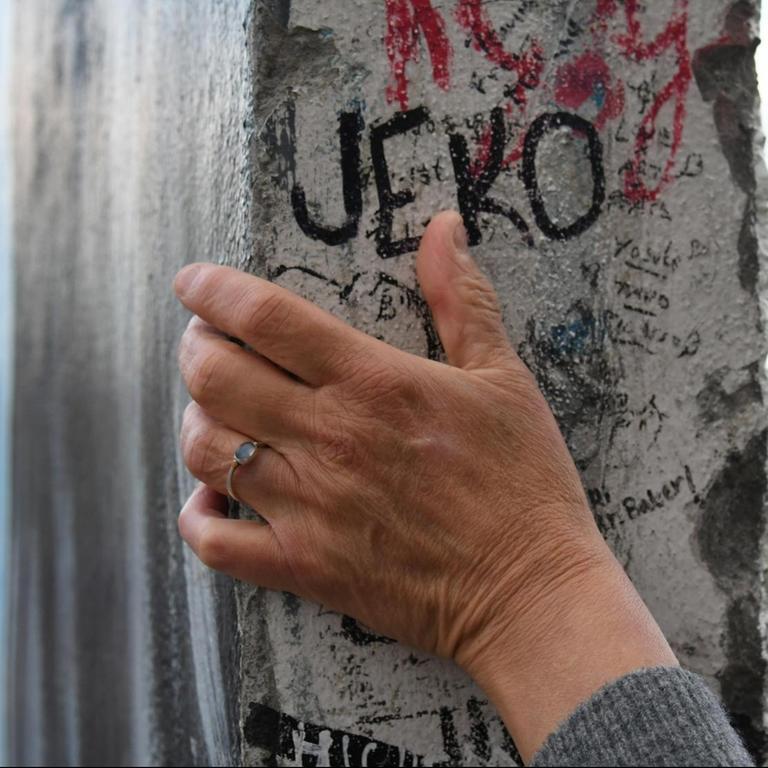 Eine Hand umgreift ein erhaltenes Teilstück der Berliner Mauer